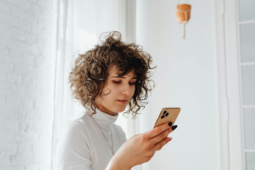 woman in white turtleneck looking at her phone