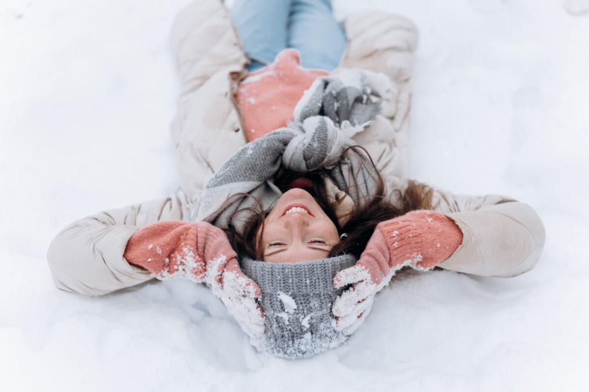 Woman laying in the snow wearing a long puffer coat